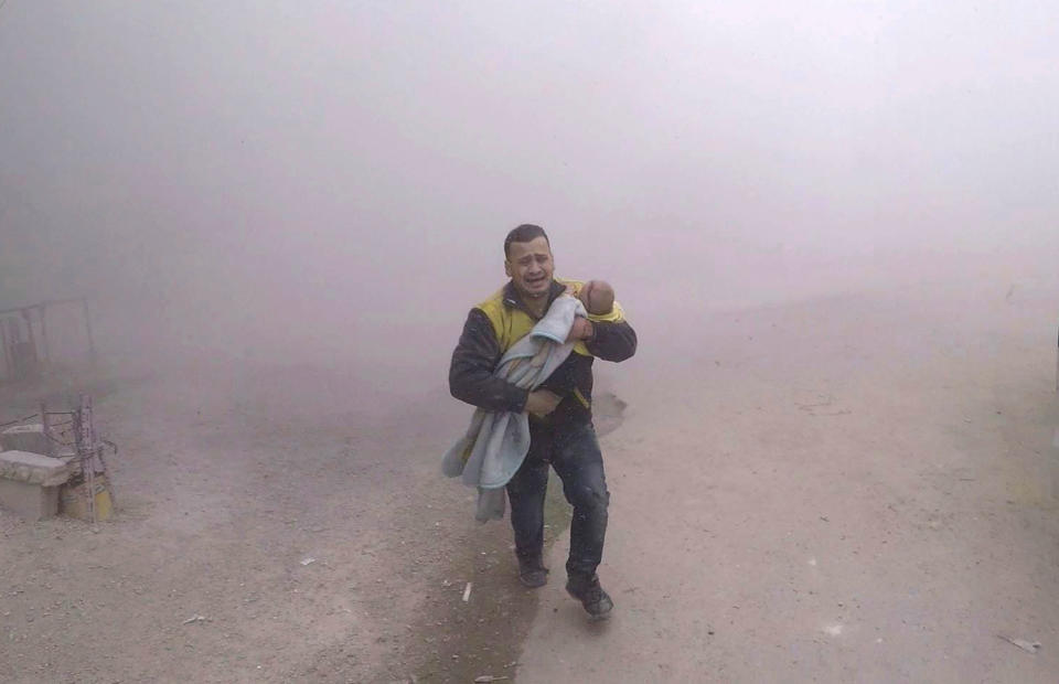 <p>A Syrian Civil Defense group, known as the White Helmets, paramedic carries his wounded son fleeing from the scene of an attack after airstrikes hit a rebel-held suburb near Damascus, Syria, Tuesday, Feb. 6, 2018. (Photo: Syrian Civil Defense White Helmets via AP) </p>