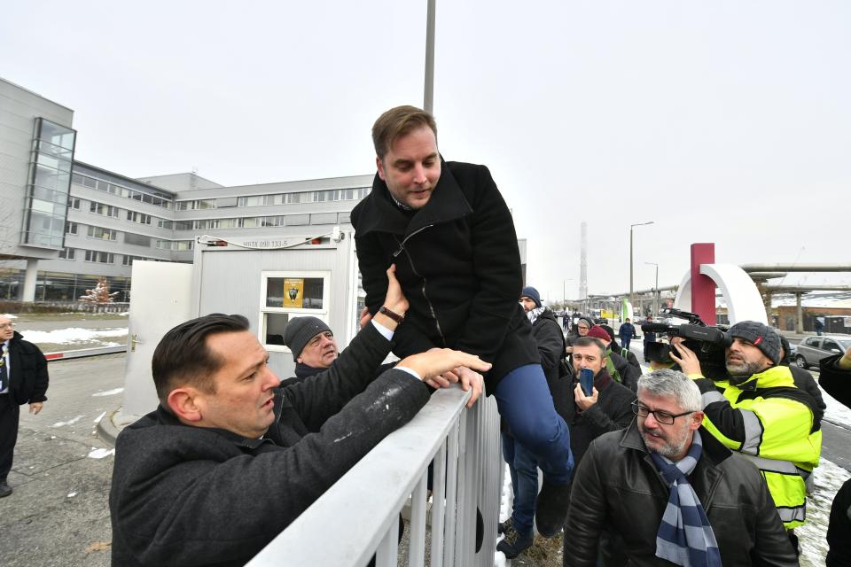 Parliamentary deputy of the oppositional Hungarian Socialist Party MSZP Zsolt Molnar, left, helps MSZP deputy Tamas Harangozo climb the fence of the public broadcaster MTVA in Budapest, Hungary, Monday, Dec. 17, 2018. Oppositional lawmakers protest against the amendments to the labour code adopted on Dec. 12, and insist to read out their demands live in the public media. (Zsolt Szigetvary/MTI via AP)