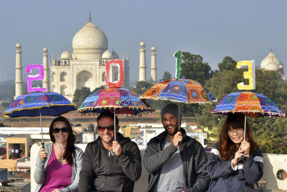 Tourists pose as they carry umbrellas with numbers to welcome the New Year 2013 on the terrace of a hotel in the backdrop of Taj Mahal in Agra, India, Monday, Dec. 31, 2012. (AP Photo/Pawan Sharma)