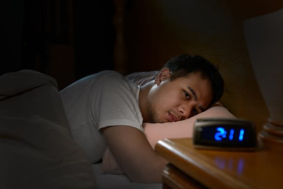 Man lying in bed in a dark room with eyes open