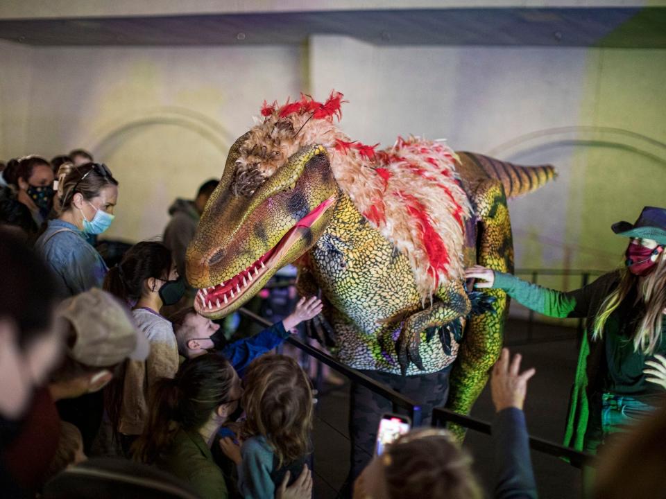 People gather around an animatronic of an Utah Raptor in an indoor's display.