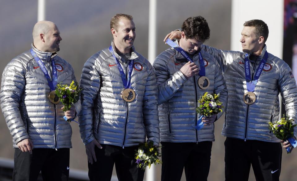 The United States' Christopher Fogt adjusts the medal of Steven Langton as they and driver Steven Holcomb, left, and Curtis Tomasevicz with USA-1 receive their bronze medals after the men's four-man bobsled competition final at the 2014 Winter Olympics, Sunday, Feb. 23, 2014, in Krasnaya Polyana, Russia.(AP Photo/Natacha Pisarenko)