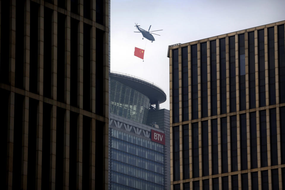 A helicopter carrying the Chinese flag flies above the central business district in Beijing, Sunday, Sept. 15, 2019. Many of the streets in the central part of China's capital were shut down this weekend for a rehearsal for what is expected to be a large military parade on Oct. 1 to commemorate the 70th anniversary of Communist China. (AP Photo/Mark Schiefelbein)