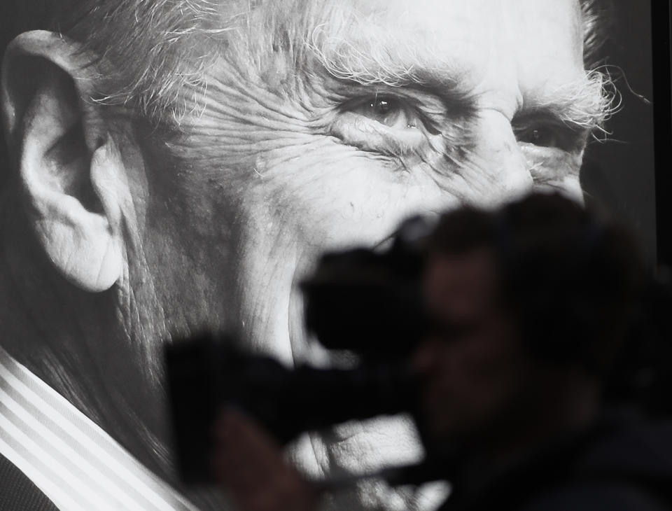 A TV camera is silhouetted against a portrait of Prince Philip in Windsor, England, Friday, April 16, 2021. Prince Philip husband of Britain's Queen Elizabeth II died April 9, aged 99, his funeral will take place Saturday at Windsor Castle in St George's Chapel. (AP Photo/Alastair Grant)