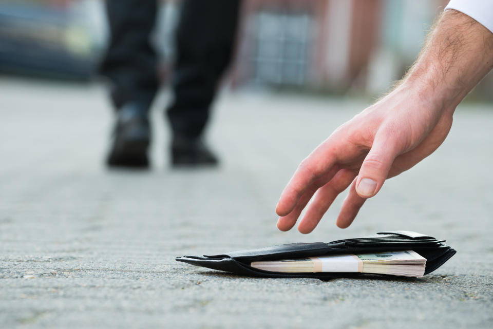 Cropped hand of businessman picking up fallen wallet with money on street