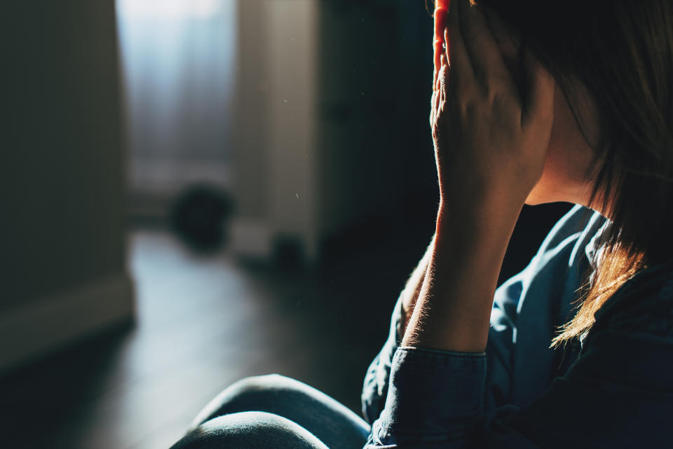 A person holding their face in their hands, sitting indoors in a dimly lit room, suggesting feelings of distress or contemplation