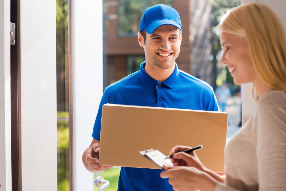 A smiling woman signing for a package being delivered by a man in a blue uniform.