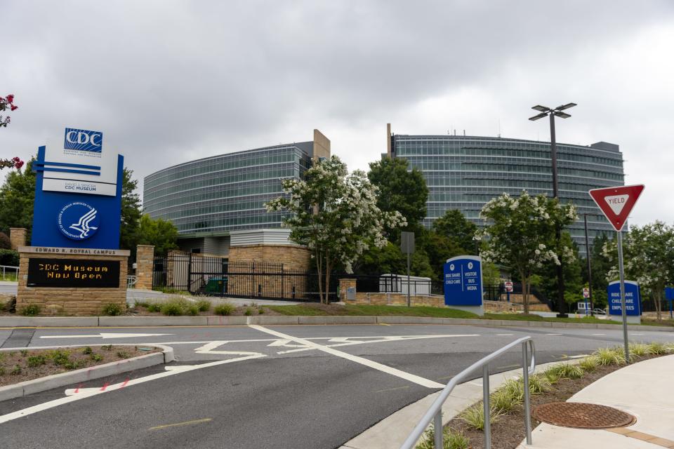 A curving glass building, maybe 10 stories, in an office park, with a sign reading "US Centers for Disease Control and Prevention"