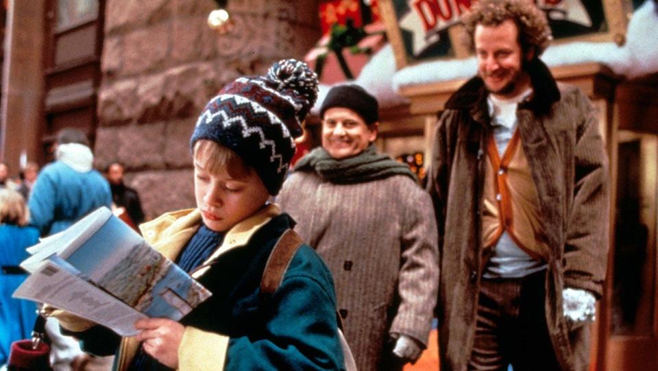 Macaulay Culkin reading a map while Joe Pesci and Daniel Stern are smiling behind him