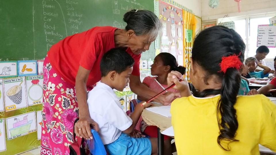 Maestra corrigiendo el trabajo de un niño en una escuela en Tuvalu