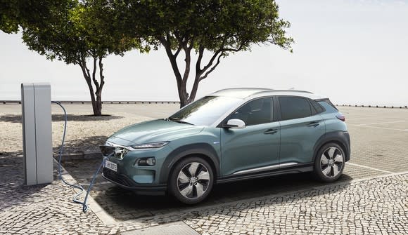 A green Hyundai Kona Electric, a small crossover SUV, parked at a charging station.