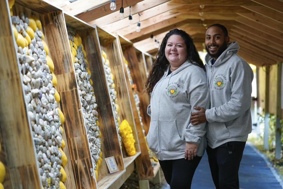 Rima Samman and her partner Travis Whitaker pose for a picture at Rami's Heart COVID-19 Memorial in Wall Township, N.J., Wednesday, Oct. 27, 2021. The memorial, which started out on a jersey shore beach made of shells and rocks, has found a permanent home at Allaire Community Farm. Started by Rima Samman and named after her brother Rami, who was killed by the coronavirus, it has grown to more than 4,000 victims' names, with dozens of new names added every week. (AP Photo/Seth Wenig)