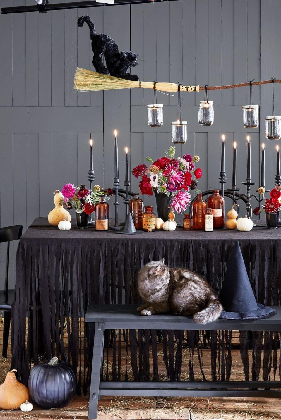 <p>Go all out with apothecary bottles, gourds, flowers and black candles lining the center of your table. A black cat sitting atop a witch's broom suspended from the ceiling takes it over the top.</p>