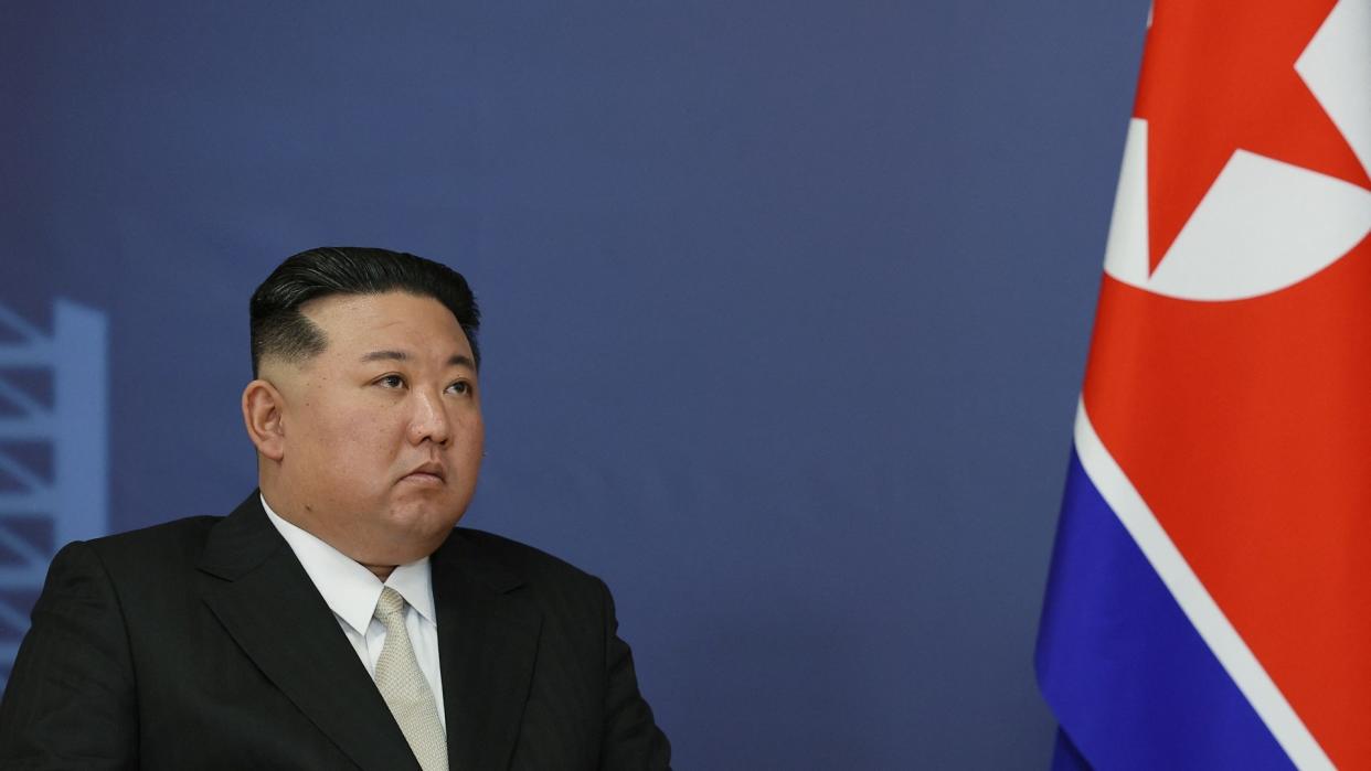  North korean leader kim jong un sits beside the nation's flag. 