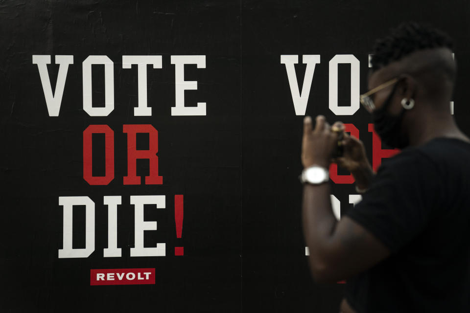 A woman stands in front of a commercial advertisement with a political message urging people to vote in Los Angeles, Wednesday, Oct. 21, 2020. (AP Photo/Jae C. Hong)