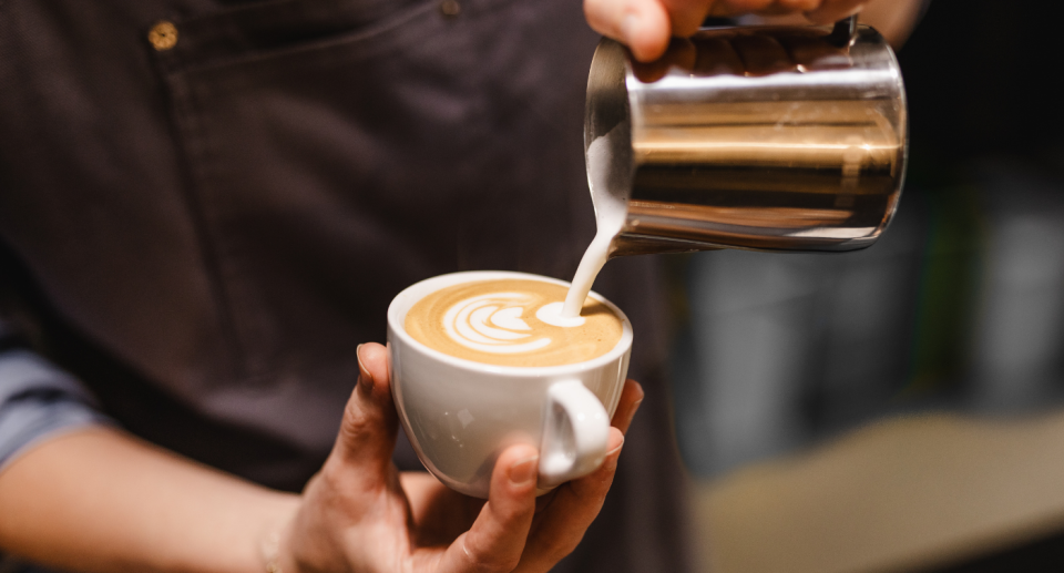 Barista at cafe pouring milk into coffee