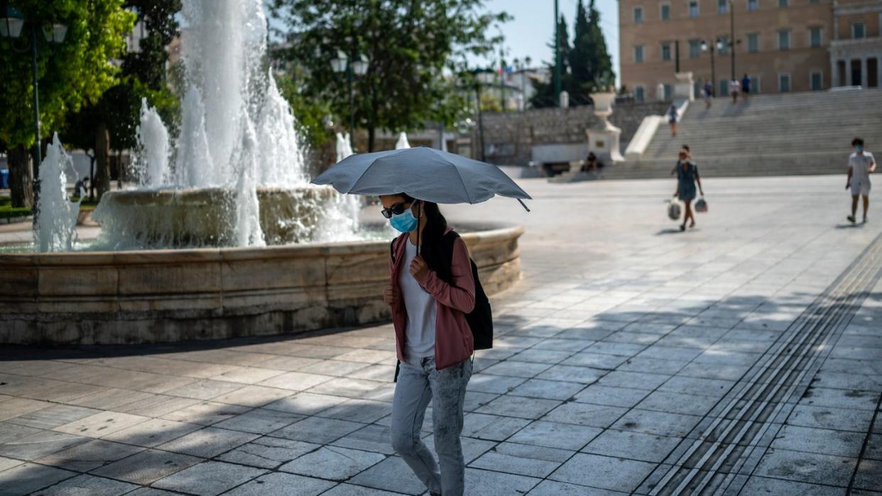 Eine Frau schützt sich bei Temperaturen über 40 Grad in Athen mit einem Schirm vor Sonne und Hitze.