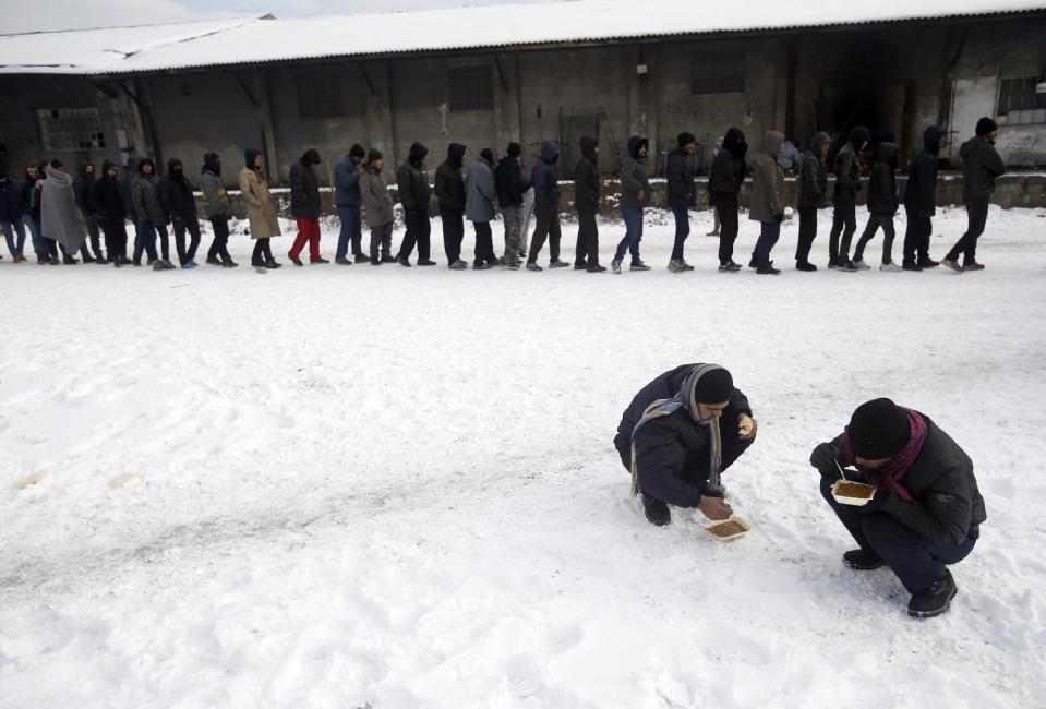 In this Thursday, Jan. 12, 2017 photo, migrants squat in the snow as they eat warm meals distributed by aid groups as others queue for their portion outside a crumbling warehouse that has served as a makeshift shelter in Belgrade, Serbia. It was a week in frigid hell for hundreds of migrants squatting in an abandoned warehouse in the Serbian capital of Belgrade while trying to move on toward Western Europe. (AP Photo/Darko Vojinovic)