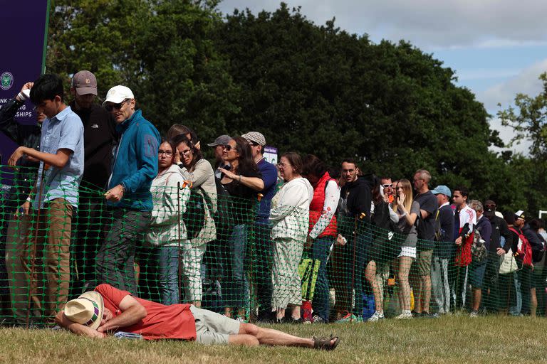 Un hombre duerme en el césped mientras la gente hace cola para entrar en el All England; hubo caos y filas interminables para ver el torneo de Wimbledon