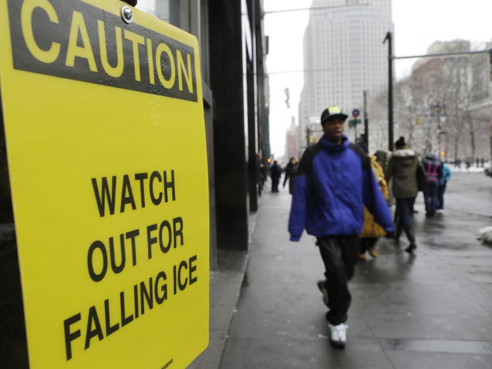 Pedestrians pass a sign warning them of falling ice near City Hall Tuesday, Feb. 18, 2014, in New York. Amid a brutal winter, New Yorkers are battling something far more dangerous than snow falling from the sky: ice tumbling from skyscrapers. (AP Photo/Frank Franklin II)