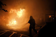 A firefighter tries to put off a fire on the street during clashes between protestors and police in Barcelona, Spain, Wednesday, Oct. 16, 2019. Spain's government said Wednesday it would do whatever it takes to stamp out violence in Catalonia, where clashes between regional independence supporters and police have injured more than 200 people in two days. (AP Photo/Emilio Morenatti)
