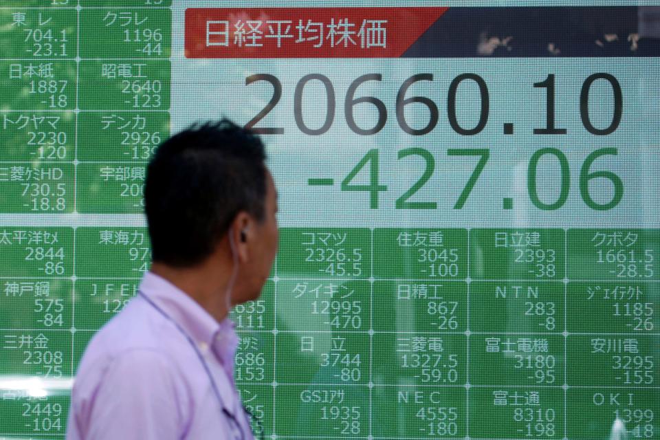 A man walks past an electronic stock board showing Japan's Nikkei 225 index at a securities firm in Tokyo Monday, Aug. 5, 2019.