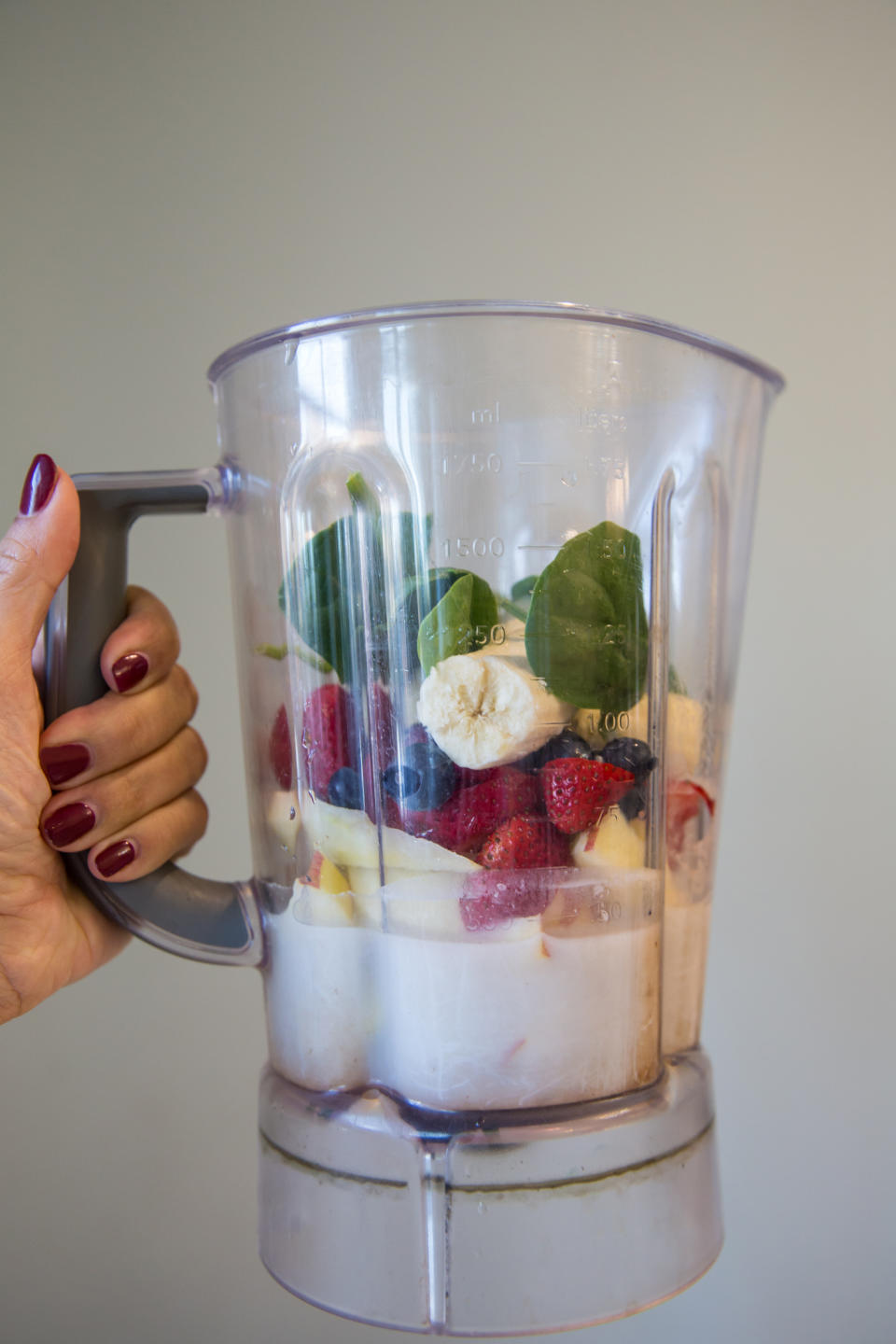 Hand holding a blender with various fruits and spinach, ready to mix