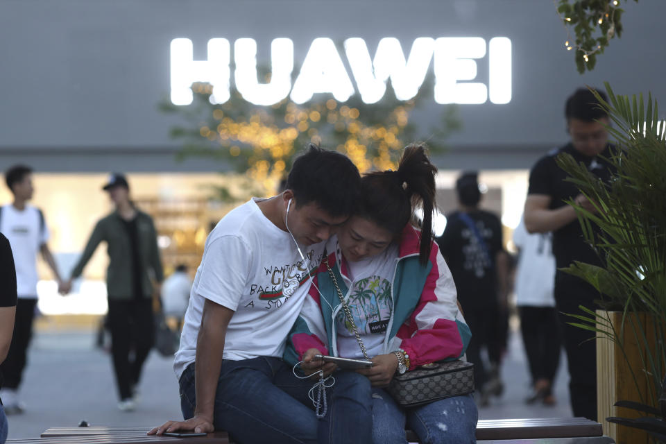 In this Monday, May 20, 2019, photo, a couple watch content on a smartphone near a Huawei store in Beijing. Chinese tech giant Huawei has filed a motion in U.S. court challenging the constitutionality of a law that limits its sales of telecom equipment. (AP Photo/Ng Han Guan)