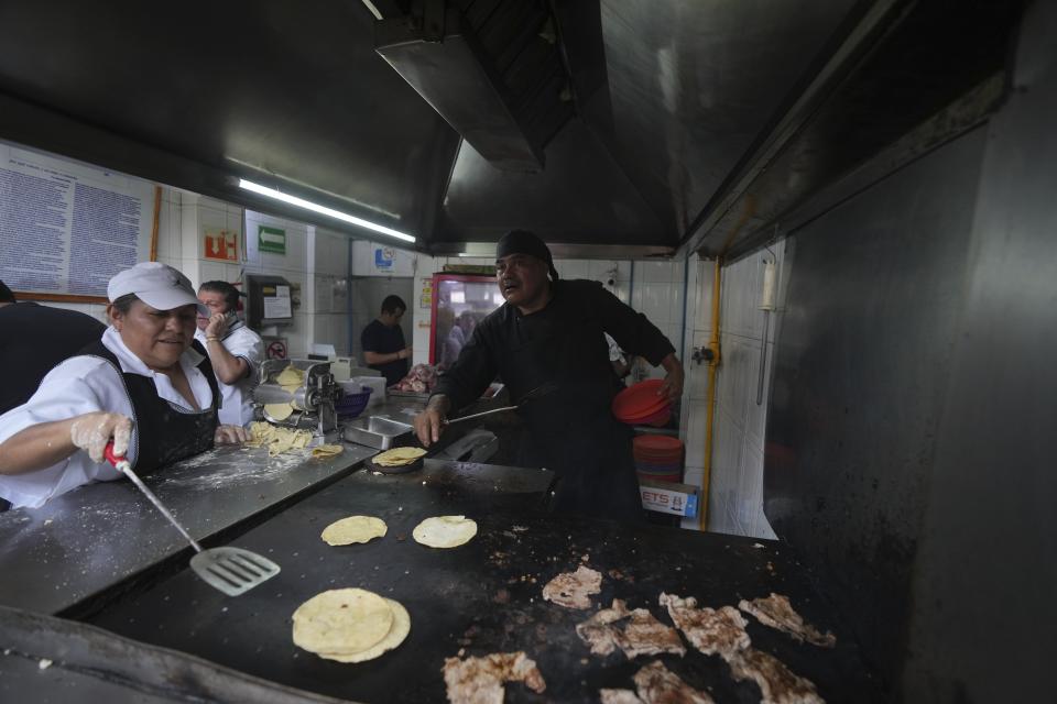 El chef Arturo Rivera Martínez, recién galardonado con una estrella Michelin, agarra varios platos mientras una ayudante calienta las tortillas de maíz en una plancha en la taquería Tacos El Califa de León en Ciudad de México, el miércoles 15 de mayo de 2024. Tacos El Califa de León es la primera taquería en recibir una estrella Michelin. (AP Foto/Fernando Llano)