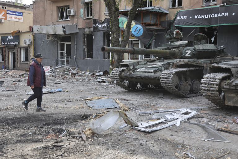 Una mujer camina frente a tanques de las fuerzas armadas de la República Popular de Donetsk, en Mariúpol, territorio bajo el gobierno de la República Popular de Donetsk, el miércoles 4 de mayo de 2022, en el este de Ucrania. (AP Foto/Alexei Alexandrov)