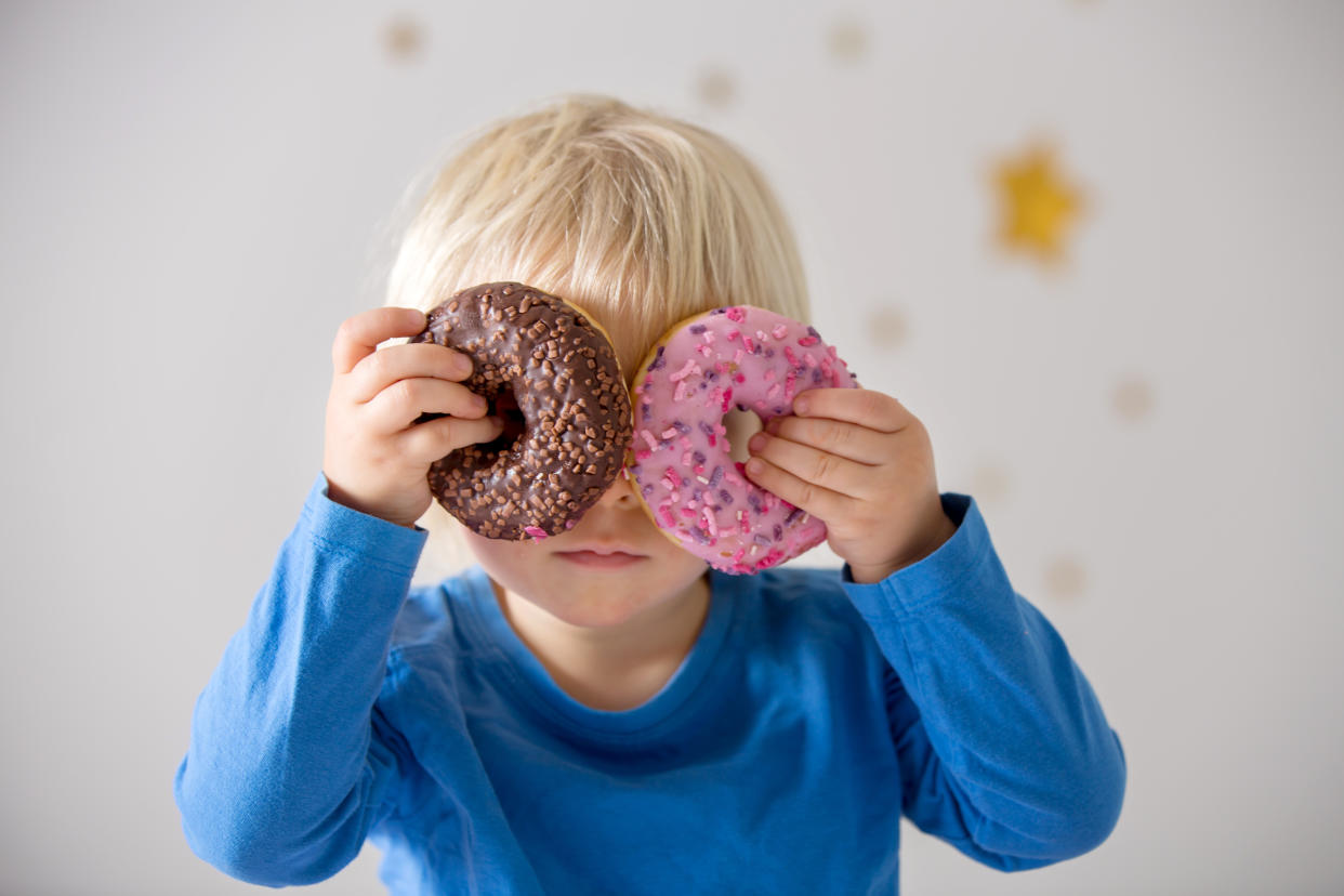 Cute sweet blonde child, playing and eating donuts at home