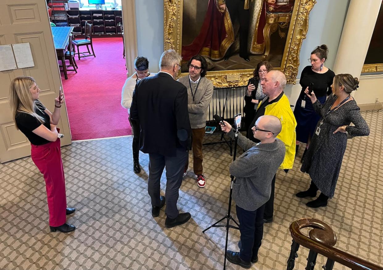 CBC reporter Michael Gorman, shown in the middle wearing glasses and a brown sweater, interviews cabinet minister John Lohr on March 21, 2024, surrounded by staff from Communications Nova Scotia and the three party caucuses.  (Jean Laroche/CBC - image credit)