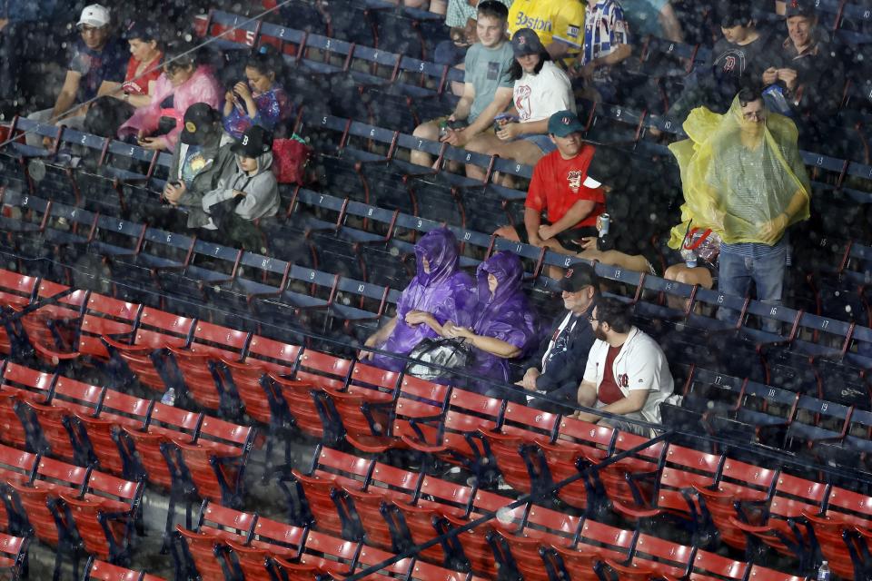 Fans take shelter during a rain delay before a baseball game between the Boston Red Sox and the Tampa Bay Rays, Friday, June 2, 2023, in Boston. (AP Photo/Michael Dwyer)