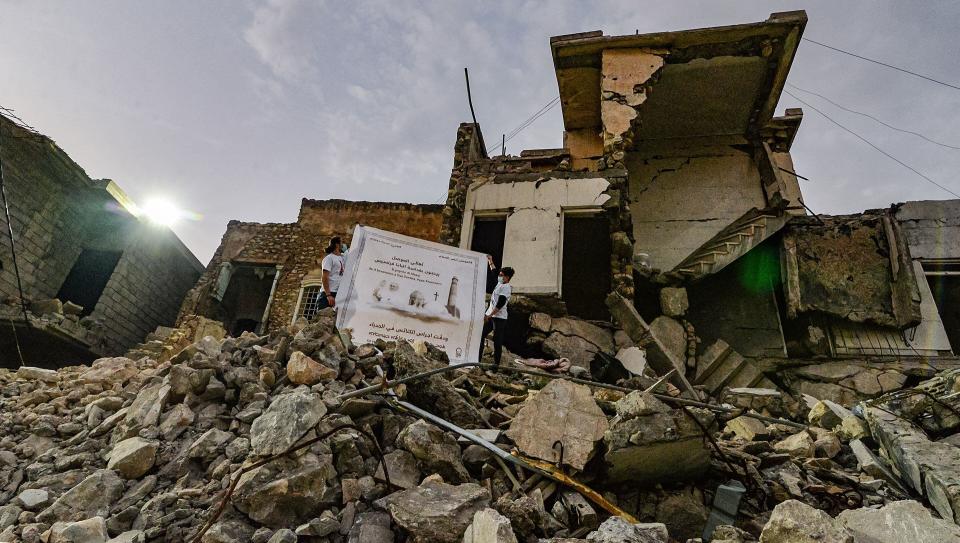 Chicos despliegan un poster de Francisco sobre los escombros de una casa destruida al lado de las ruinas de una iglesia cristiana de Mosul