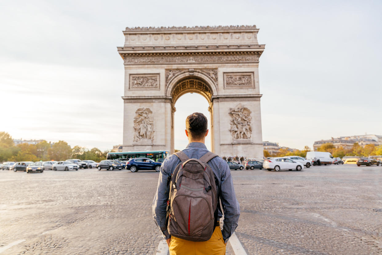 Tourist with backpack walking towards Arc de Triomphe in Paris, France