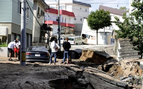 Residents watch a road damaged by an earthquake in Sapporo, Hokkaido, northern Japan - Credit: AP