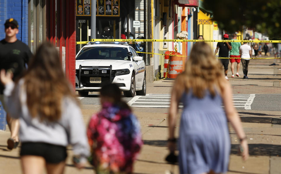 Tourists navigate police tape blocking several streets along the Virginia Beach Oceanfront on Saturday, March 27, 2021, the morning after a fatal shooting in Virginia Beach, Va. A pair of overnight fatal shootings along the beachfront in Virginia Beach wounded several people in a scene described by authorities on Saturday as “very chaotic.” (Stephen Katz /The Virginian-Pilot via AP)