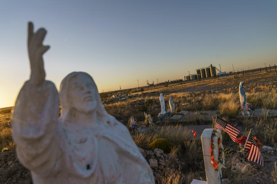 A statue of Jesus stands next to graves in a cemetery beside an oil and gas facility in Pecos, Texas, Thursday, Oct. 14, 2021. Oil was discovered here in 1921, and in the intervening century wildcatters have drilled more than a quarter million wells into the layer cake of shale rock under the desert, many more than a mile deep. (AP Photo/David Goldman)