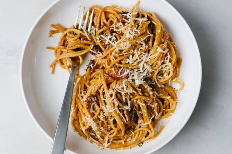 Spaghetti noodles with bacon bits and shredded cheese in bowl with fork