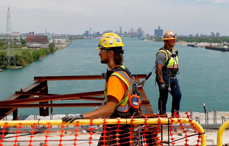 With the Detroit skyline in the background, workers on the Gordie Howe Bridge in Detroit on Tuesday, May 14, 2024, wait for parts during construction. The bridge is in the final steps of connecting the two sides, with only 85 feet remaining. The connection should be completed by the end of June.