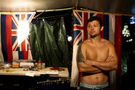 De Andre Makakoa, who lost his home to the Lahaina wildfire, poses for a portrait inside his tent at a housing protest on Kaanapali Beach Wednesday, Dec. 6, 2023, in Lahaina, Hawaii. A group of survivors is camping on the resort beach to protest and raise awareness for better long-term housing options for those displaced. Residents and survivors still dealing with the aftermath of the August wildfires in Lahaina have mixed feelings as tourists begin to return to the west side of Maui, staying in hotels still housing some displaced residents. (AP Photo/Lindsey Wasson)