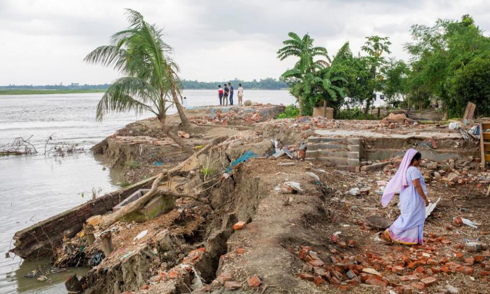 A woman walks in the ruins of a house damaged by floodwaters on a riverbank in Bangladesh