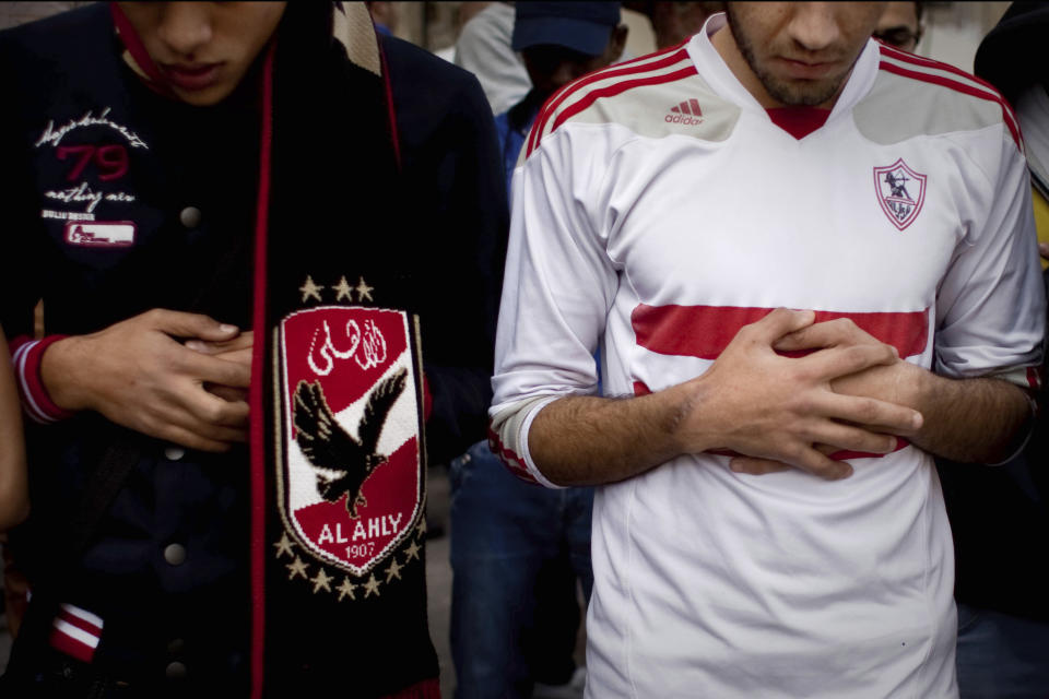 FILE - In this Feb. 9, 2015 file photo, an Ultras Al-Ahly soccer fan, left, and an Ultras White Knights soccer fan, pray for people who were killed in a riot outside a stadium, at Cairo University in Egypt. Egypt’s close relations with Saudi Arabia are being tested by a soccer spat sparked by an uproar over meddling by the kingdom’s sports minster, Turki al-Sheikh. The ongoing upheaval is destabilizing soccer in Egypt as it tries to shake off memories of the national team’s group-stage exist at the World Cup in June and the deaths of nearly 100 fans this decade. (AP Photo/Roger Anis, El Shorouk Newspaper, File)