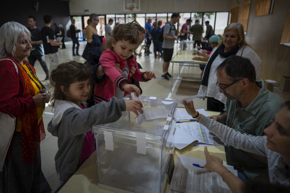 Children put their mother's ballot into the ballot box during local elections in Barcelona, Spain, Sunday, May 28, 2023. Spain goes to the polls on Sunday for local and regional elections seen as a bellwether for a national vote in December, with the conservative Popular Party (PP) steadily gaining ground on the ruling Socialists in key regions. (AP Photo/Emilio Morenatti)