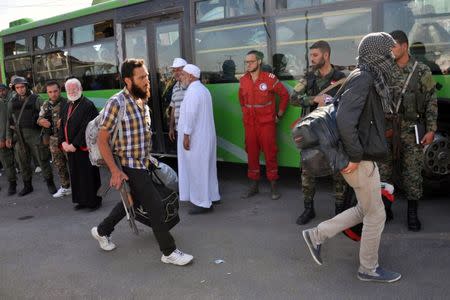 Syrian army soldiers and a member of the Syrian Arab Red Crescent look at rebel fighters walking to board a bus to evacuate the besieged Waer district in the central Syrian city of Homs, under an agreement between rebels and Syria's army, in this handout picture provided by SANA on September 26, 2016. SANA/Handout via REUTERS