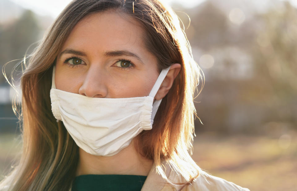 Young woman wears home made white cotton virus mouth face mask, wrong way, incorrect wearing - masks should cover nose as well