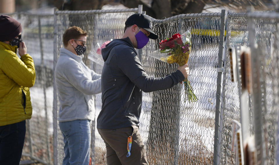 Kiefer Johnson places a bouquet of flowers into a makeshift fence put up around the parking lot outside a King Soopers grocery store where a mass shooting took place a day earlier, in Boulder, Colo., Tuesday, March 23, 2021. (AP Photo/David Zalubowski)