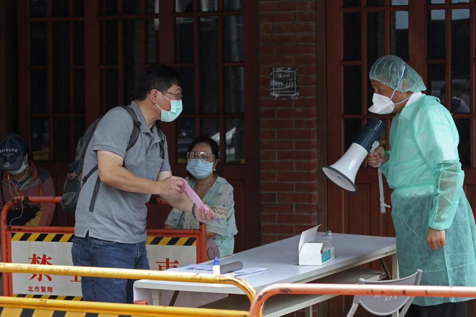 FILE - In this May 18, 2021, file photo, a medical staff wearing protective gear, guides people at a rapid coronavirus testing center after the infection alert rose to level 3 in Taipei, Taiwan. After a year of success, Taiwan is struggling with its largest outbreak since the pandemic began. When locally transmitted cases started being found in May 2021, it soon became clear that the central government was ill prepared not only to contain them, but to even detect them on a large scale due to a lack of investment in and a bias against rapid testing. (AP Photo/Chiang Ying-ying, File)