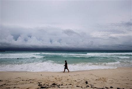 A man walks on the beach as clouds form on the horizon in Cancun October 3, 2013. REUTERS/Victor Ruiz Garcia