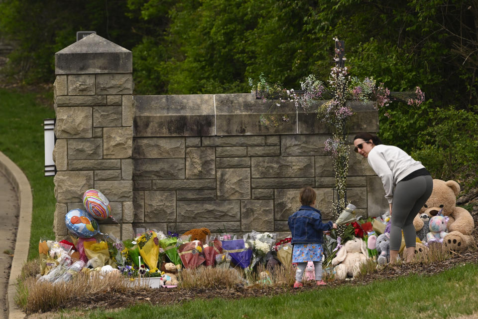 A woman and child bring flowers to lay at the entry to Covenant School which has becomes a memorial for shooting victims, Tuesday, March 28, 2023, in Nashville, Tenn. (AP Photo/John Amis)